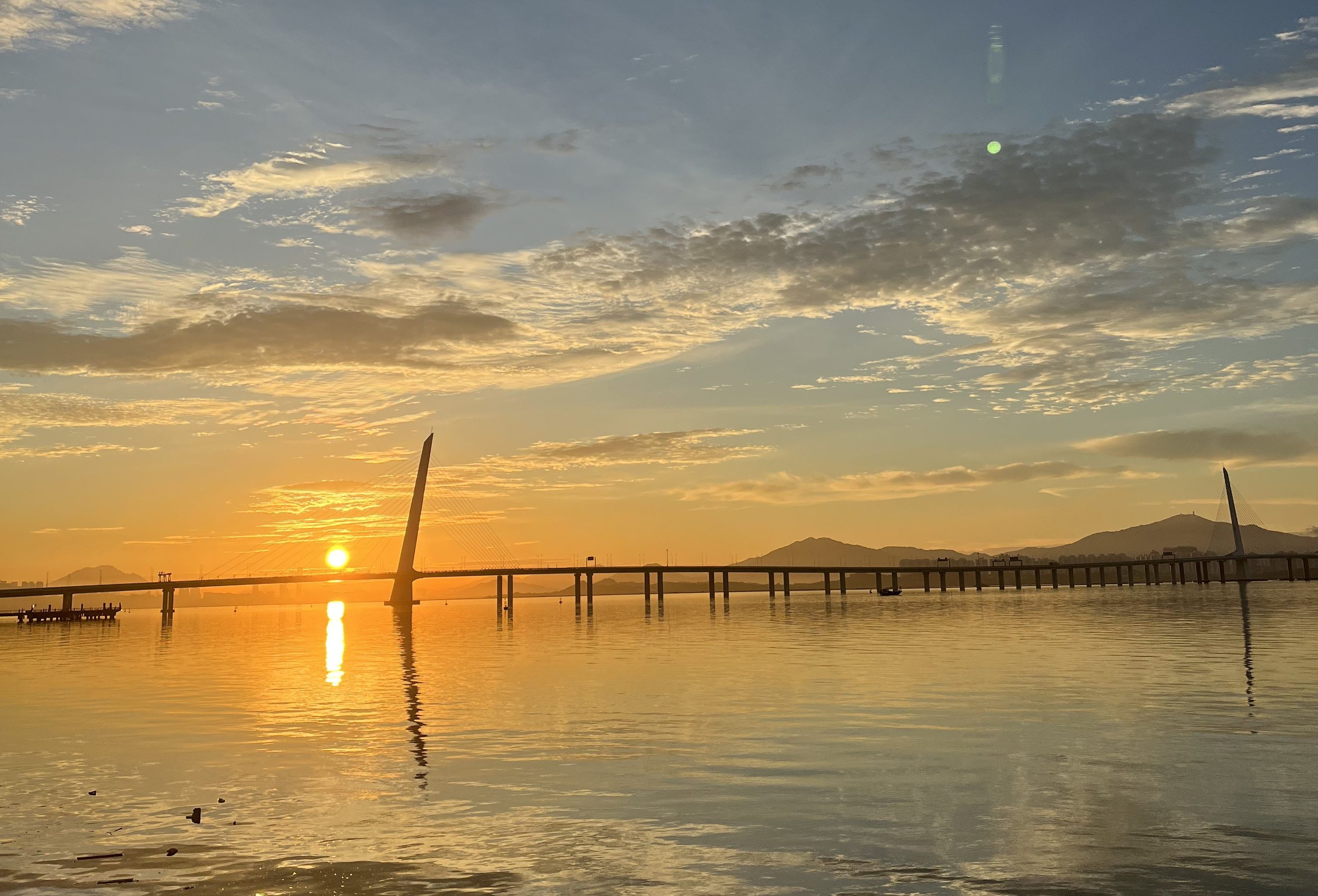 Sunrise over water with a bridge in the distance.