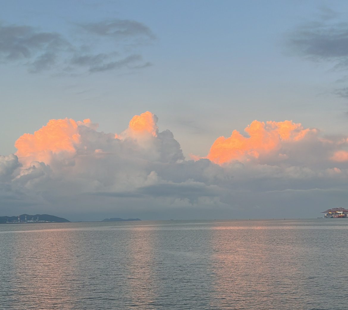 Clouds reflecting on the calm water during sunrise, with a distant coastline