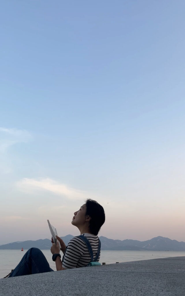 Falls looking up at the sky holding a book.