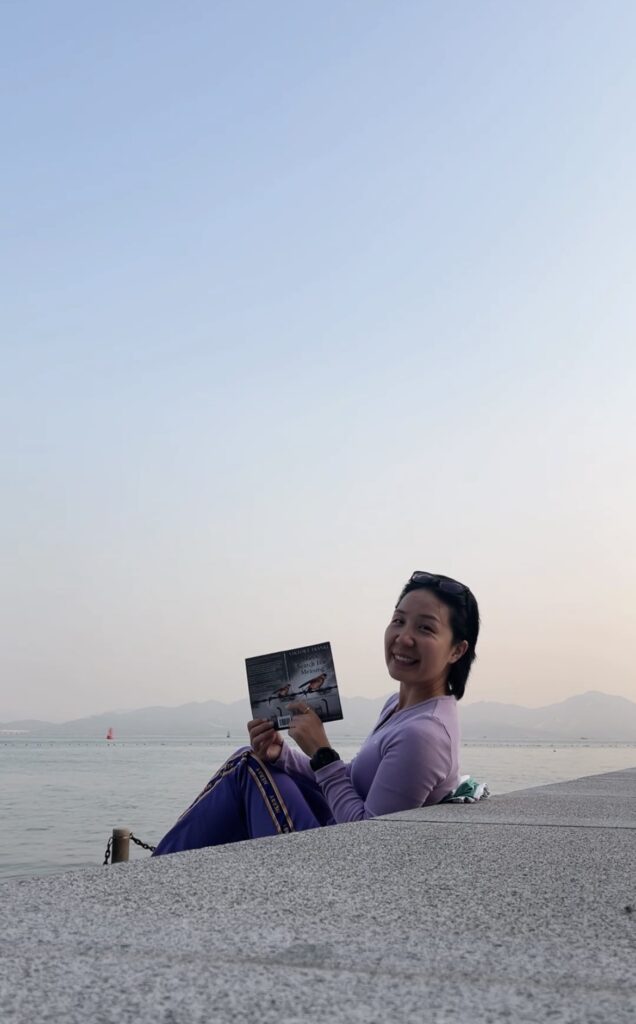 Falls holding a book sitting by the sea.