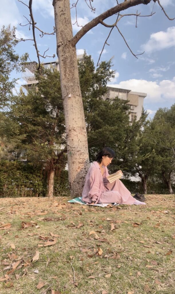 Falls reading a book under a tree wearing purple dress.