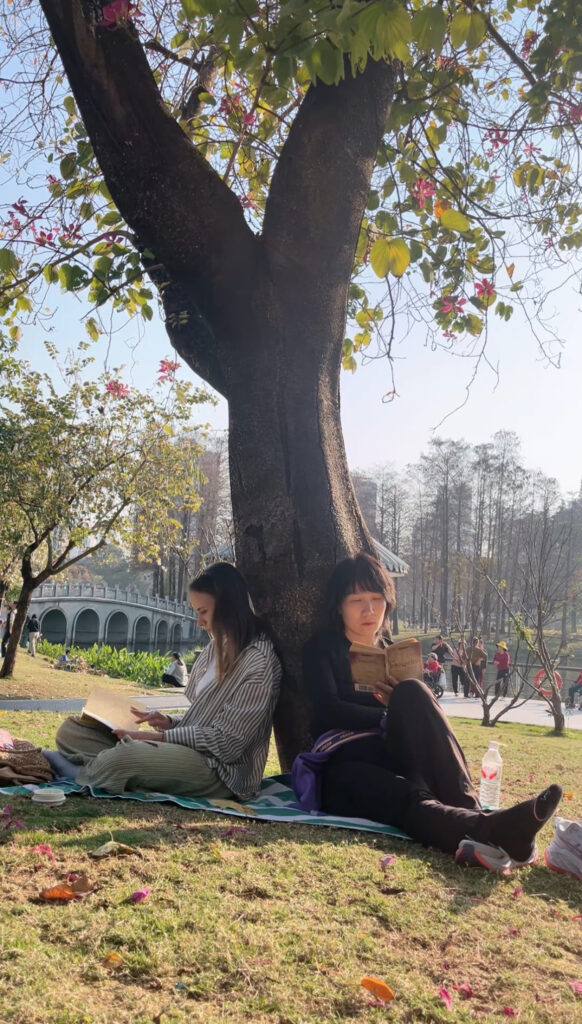 Two women reading under a flowery tree.