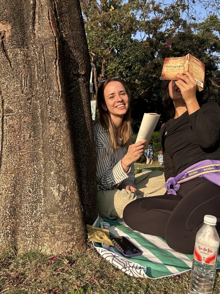 Two women holding books smile under sunshine.