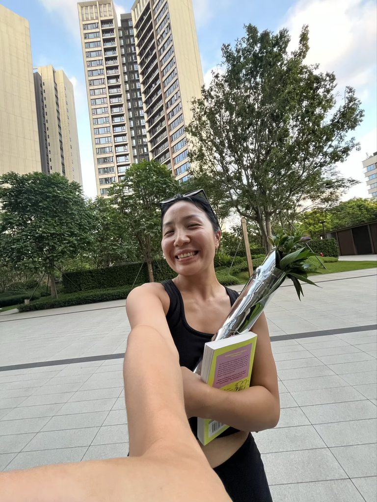 Falls taking a selfie while holding a book and a bouquet of flowers