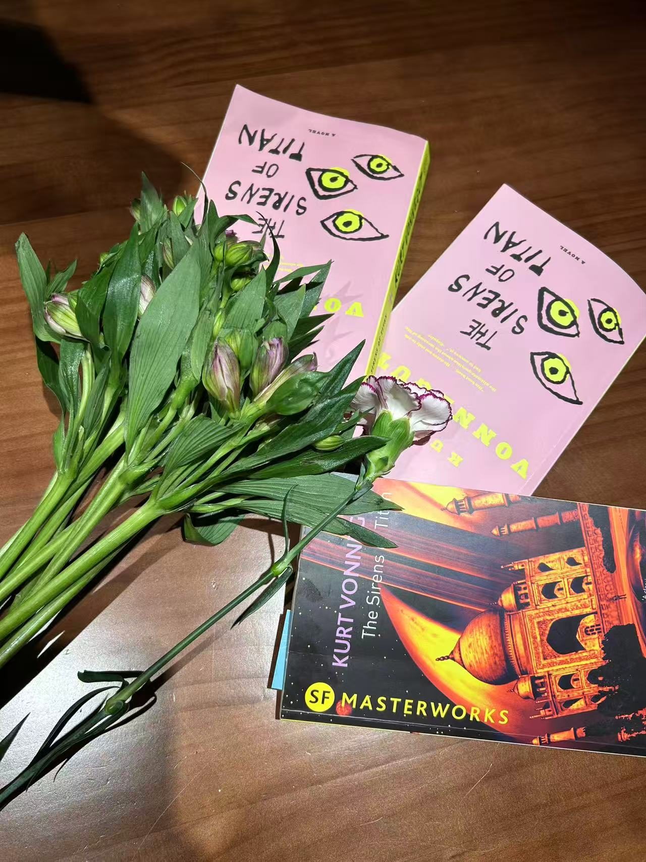 Multiple copies of The Sirens of Titan displayed on a table beside a bouquet of flowers during a Fallina book club meeting.