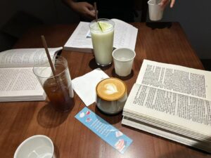 Open books spread across a table during a Fallina reading gathering, with several drinks shared among readers.