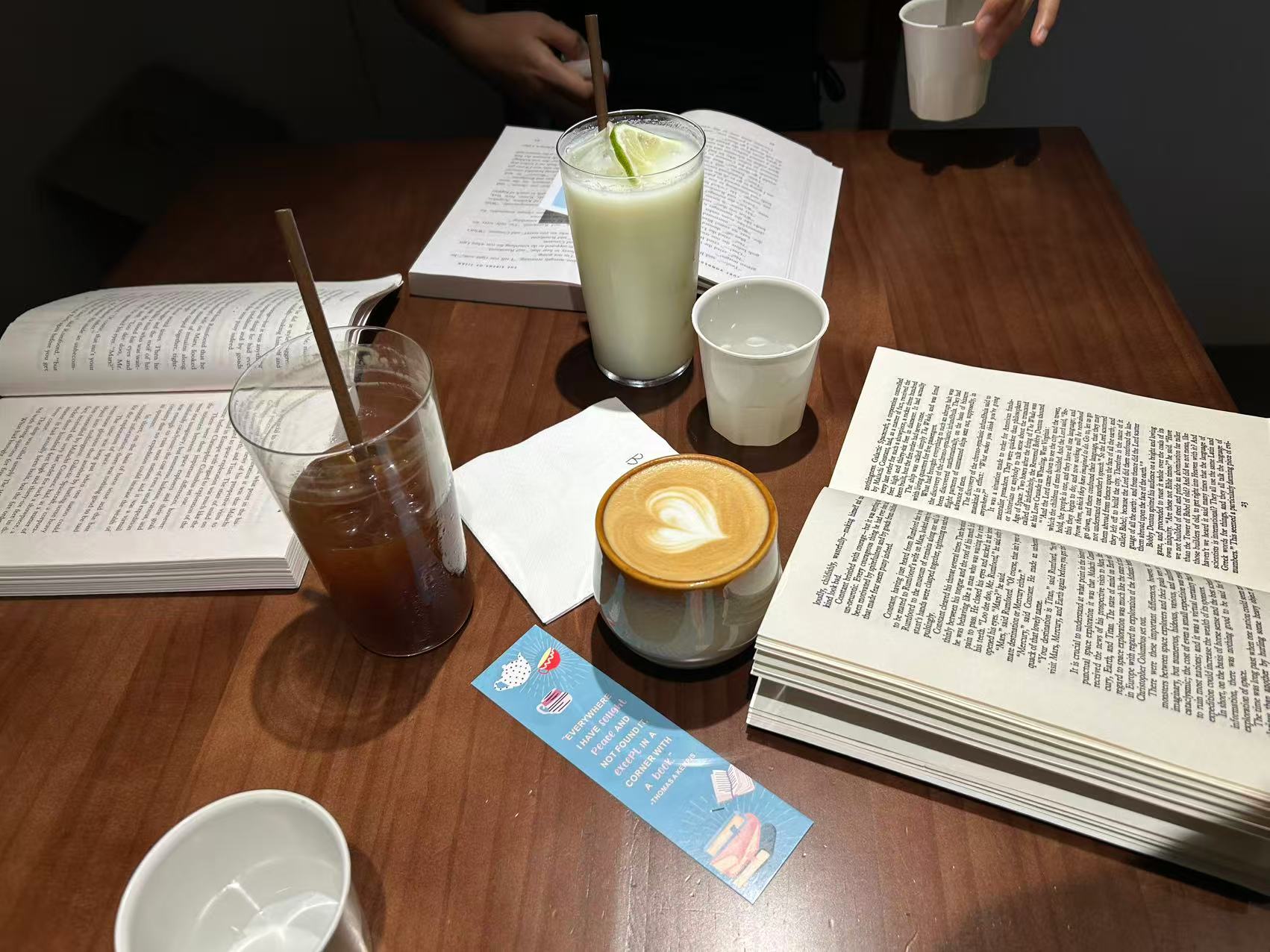Open books spread across a table during a Fallina reading gathering, with several drinks shared among readers.