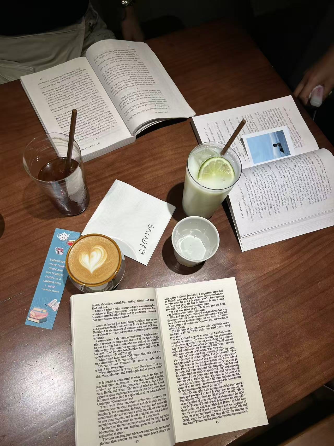 Open books spread across a table during a Fallina reading gathering, with several drinks shared among readers.