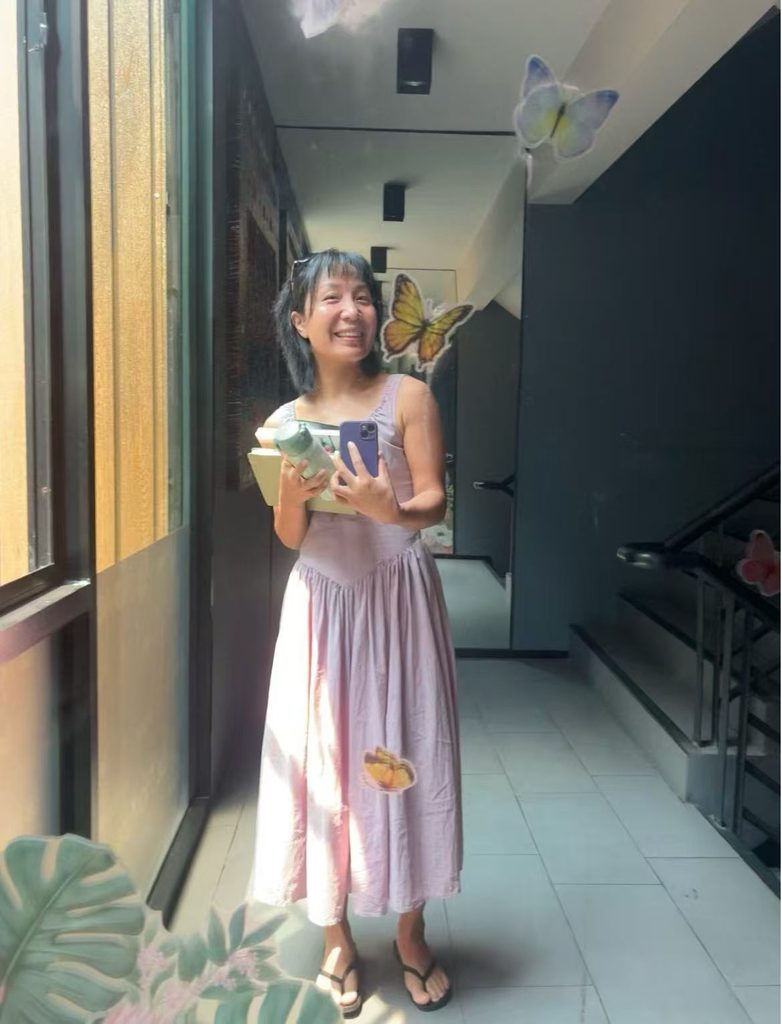 Falls holding a stack of books while taking a mirror selfie during her travels