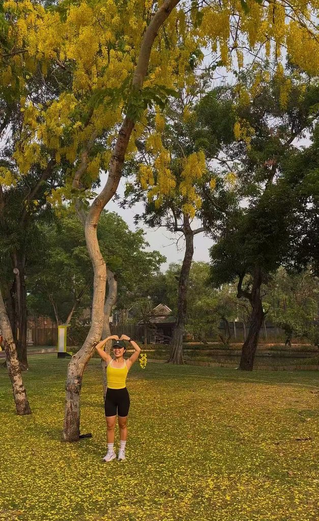 Falls making a heart sign beneath a tree full of yellow blossoms