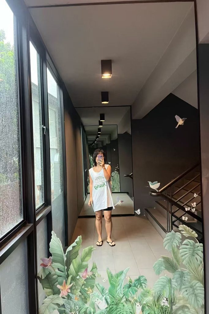 Falls taking a mirror selfie in front of a full-length mirror, holding a book 