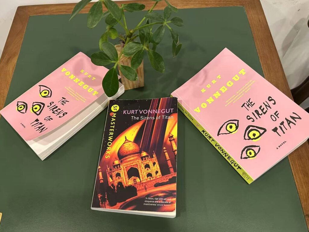 Three copies of The Sirens of Titan placed on a green table with a small green decorative plant