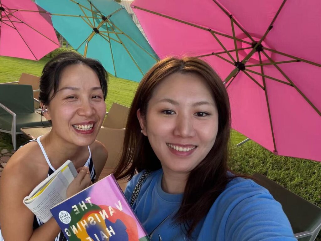 Falls and Chelsea holding books together under a colorful umbrella during their reading session