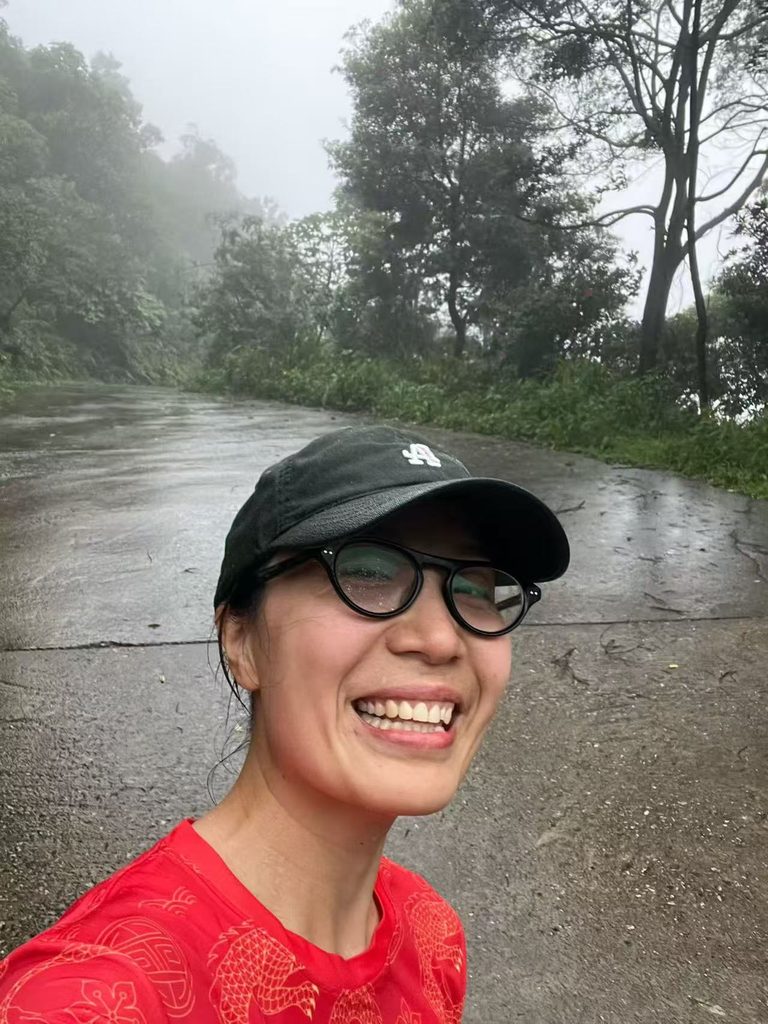 Falls smiling while hiking in the rain, with her hat and clothes soaked from the rainy