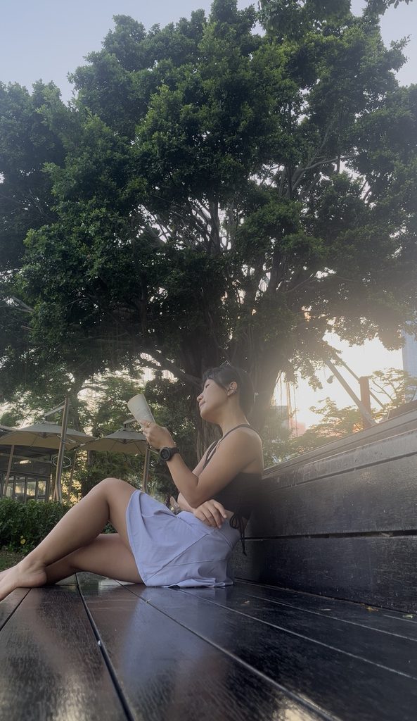 Falls reading a book on a bench under a tree during sunset, enjoying a quiet moment alone
