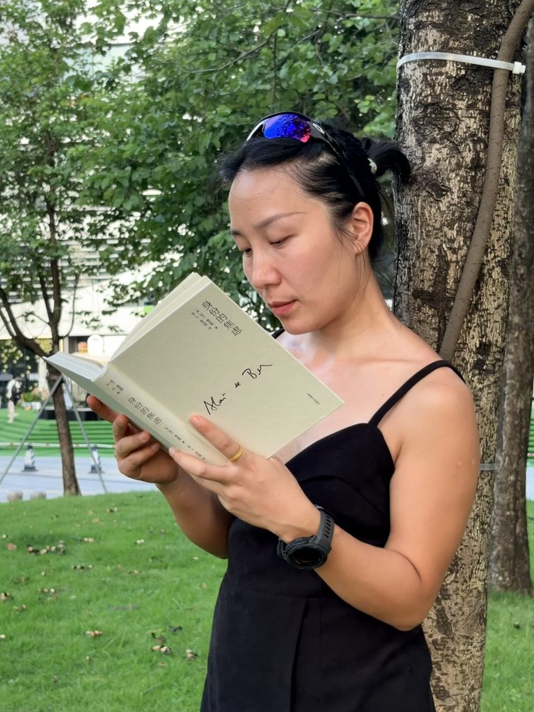 Falls reading a book while leaning against a tree