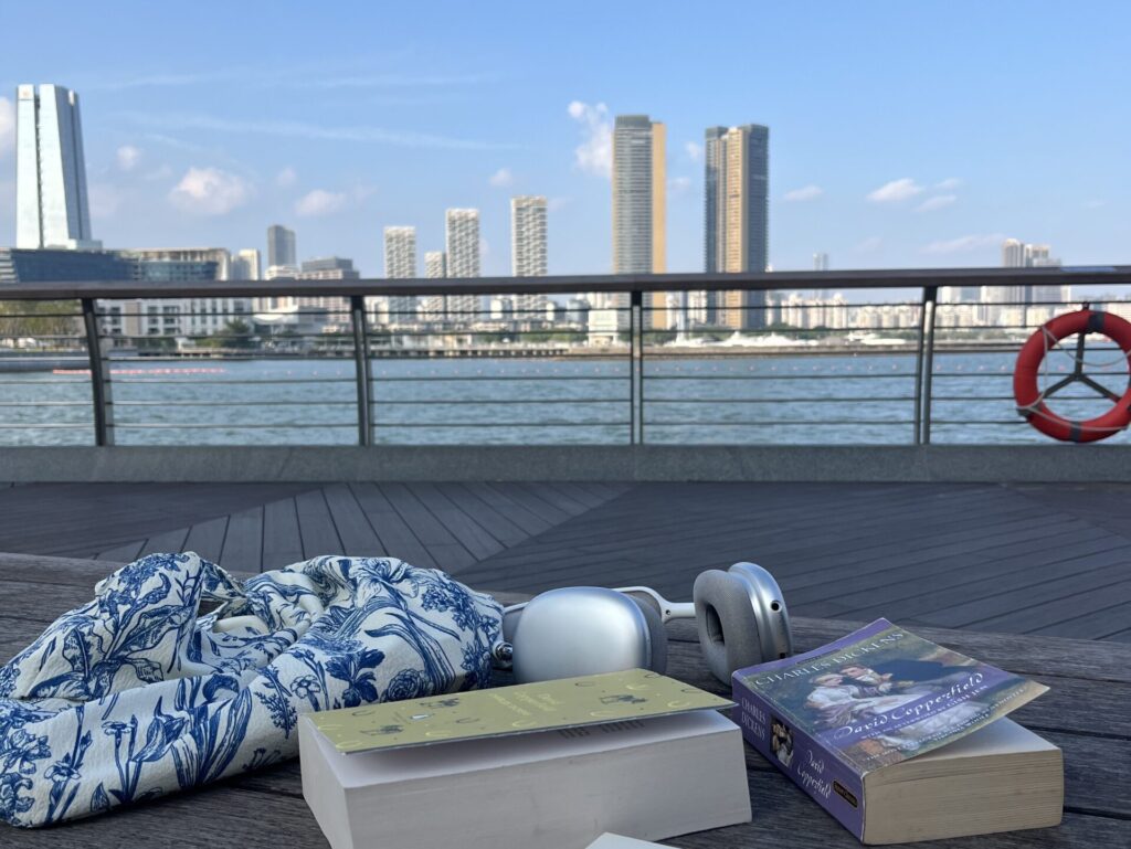 A wooden bench with books overlooking the calm ocean and city skyline in autumn, capturing a peaceful buddy read experience.